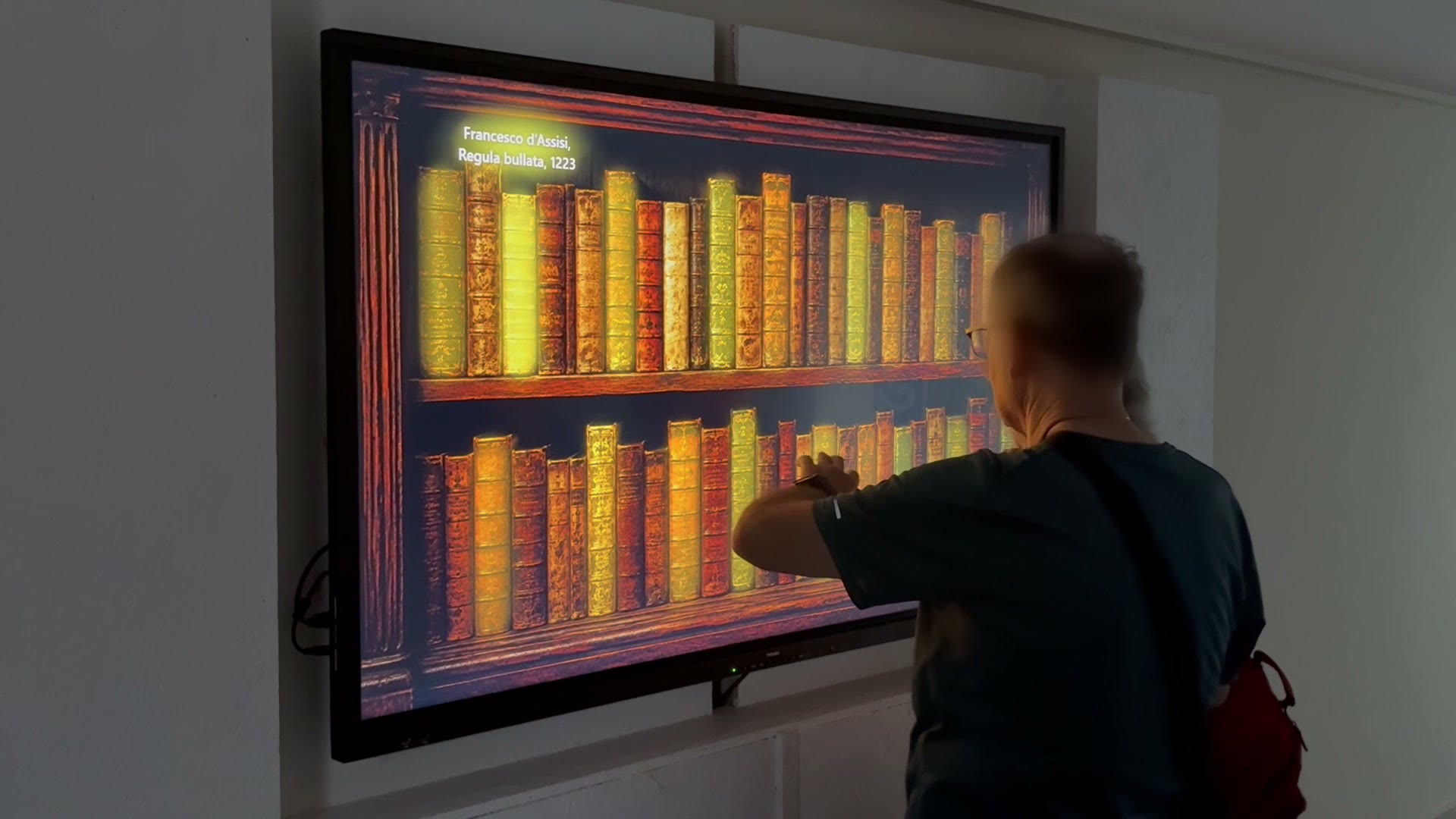 Un visitatore tocca il dorso di un volume sullo scaffale digitale di una parete touch