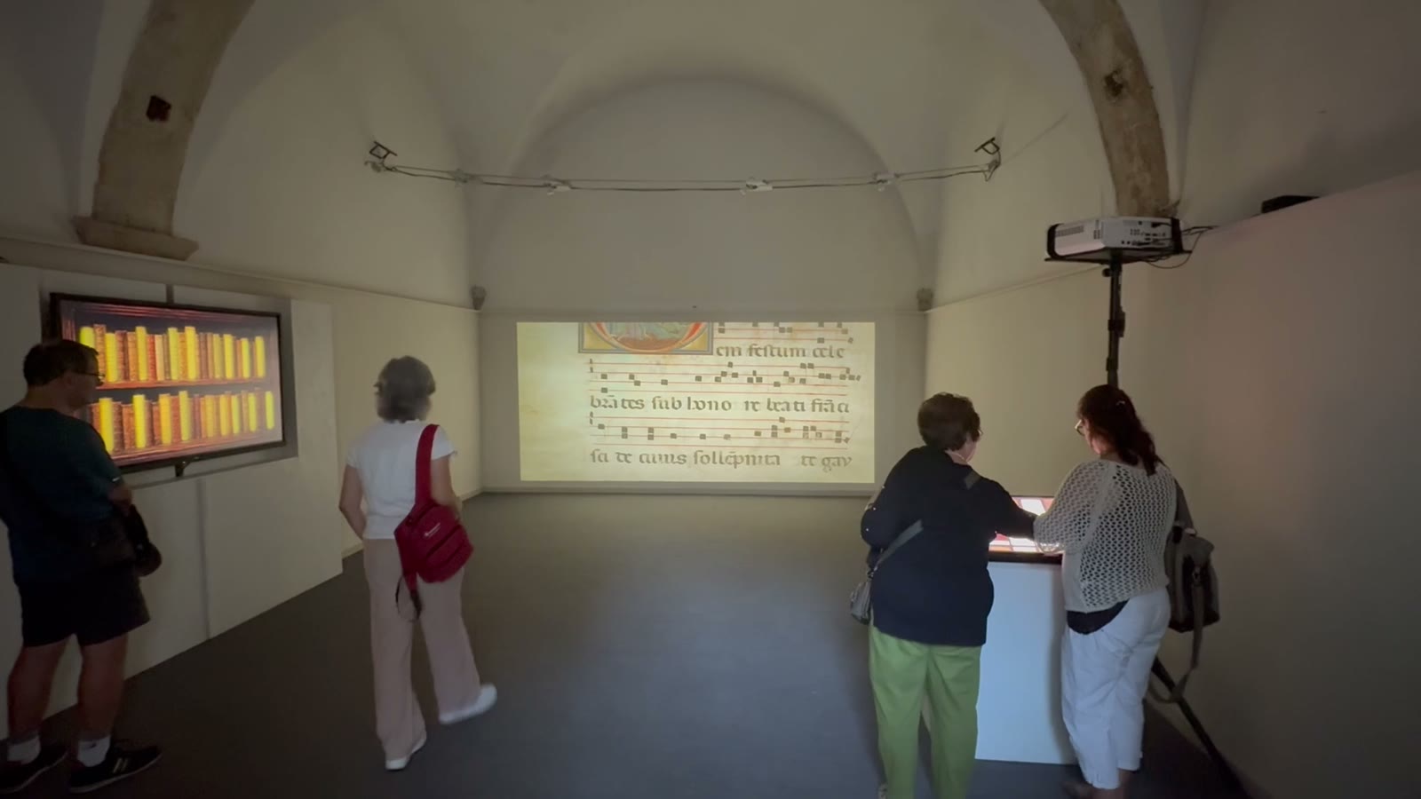 Sala espositiva con parete touch, totem e una proiezione di pagina miniata