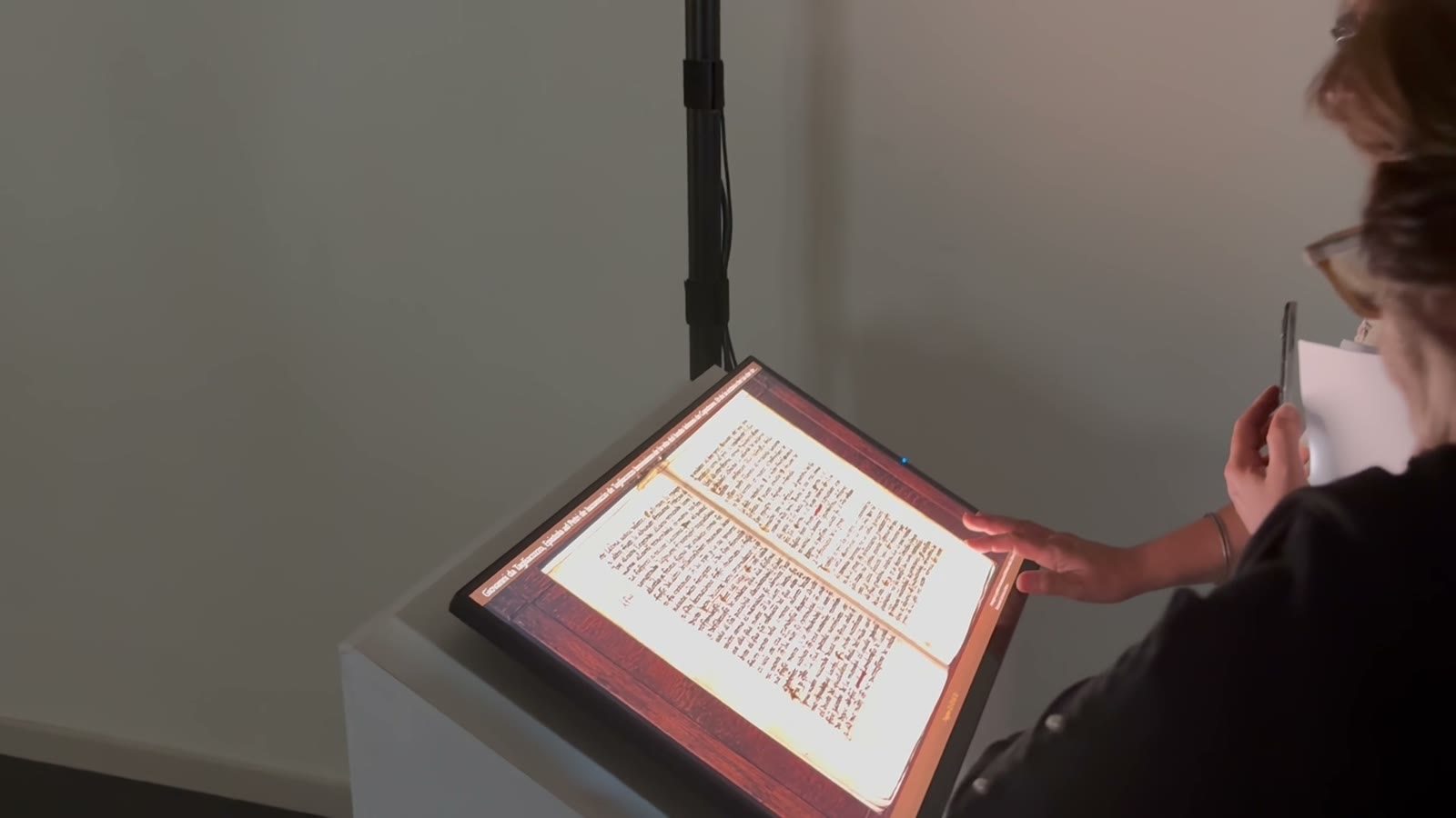 Visitatore alla postazione totem inclinata che consulta un manoscritto