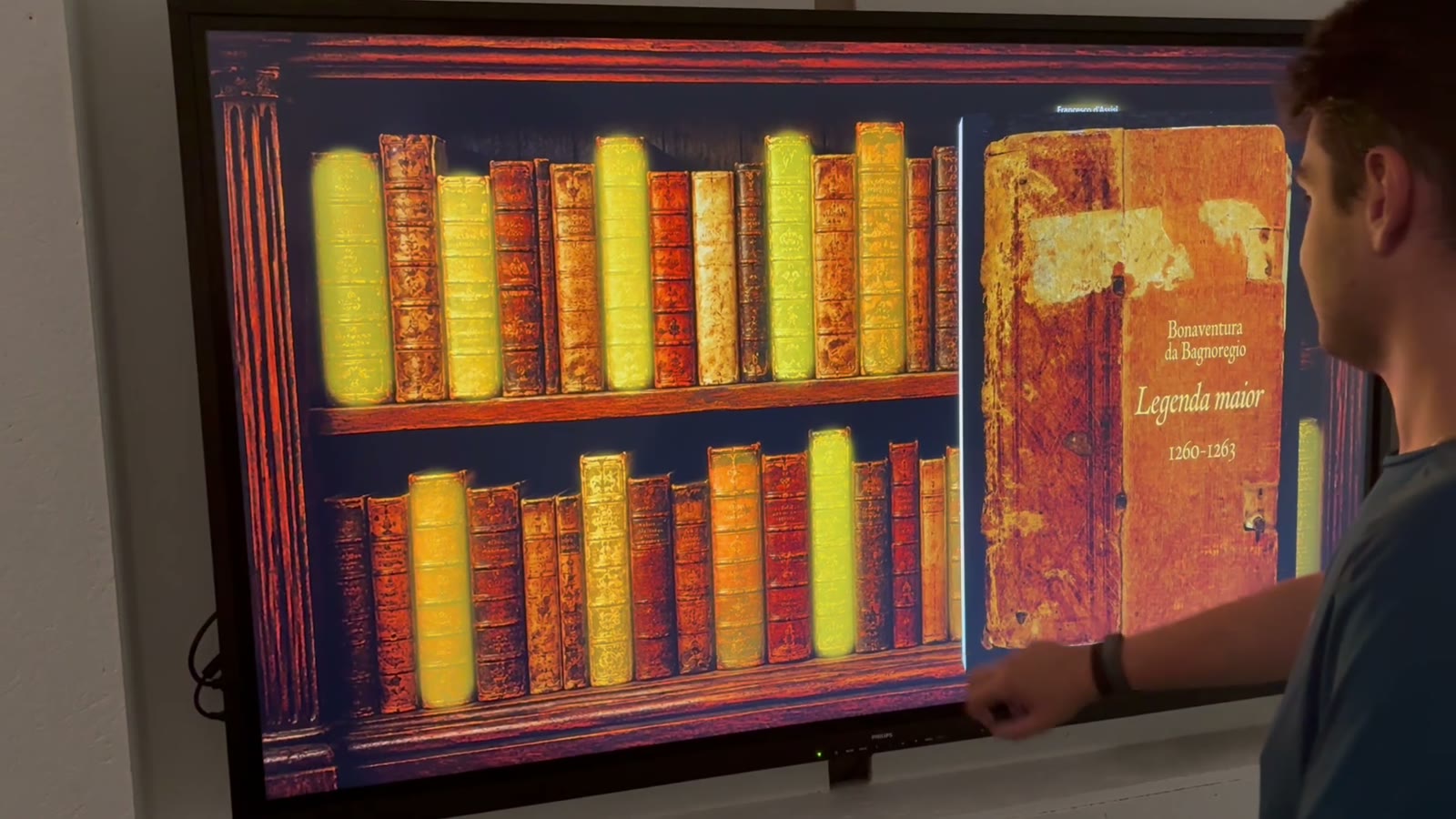 Un volume si apre in 3D sopra lo scaffale digitale di una parete touch
